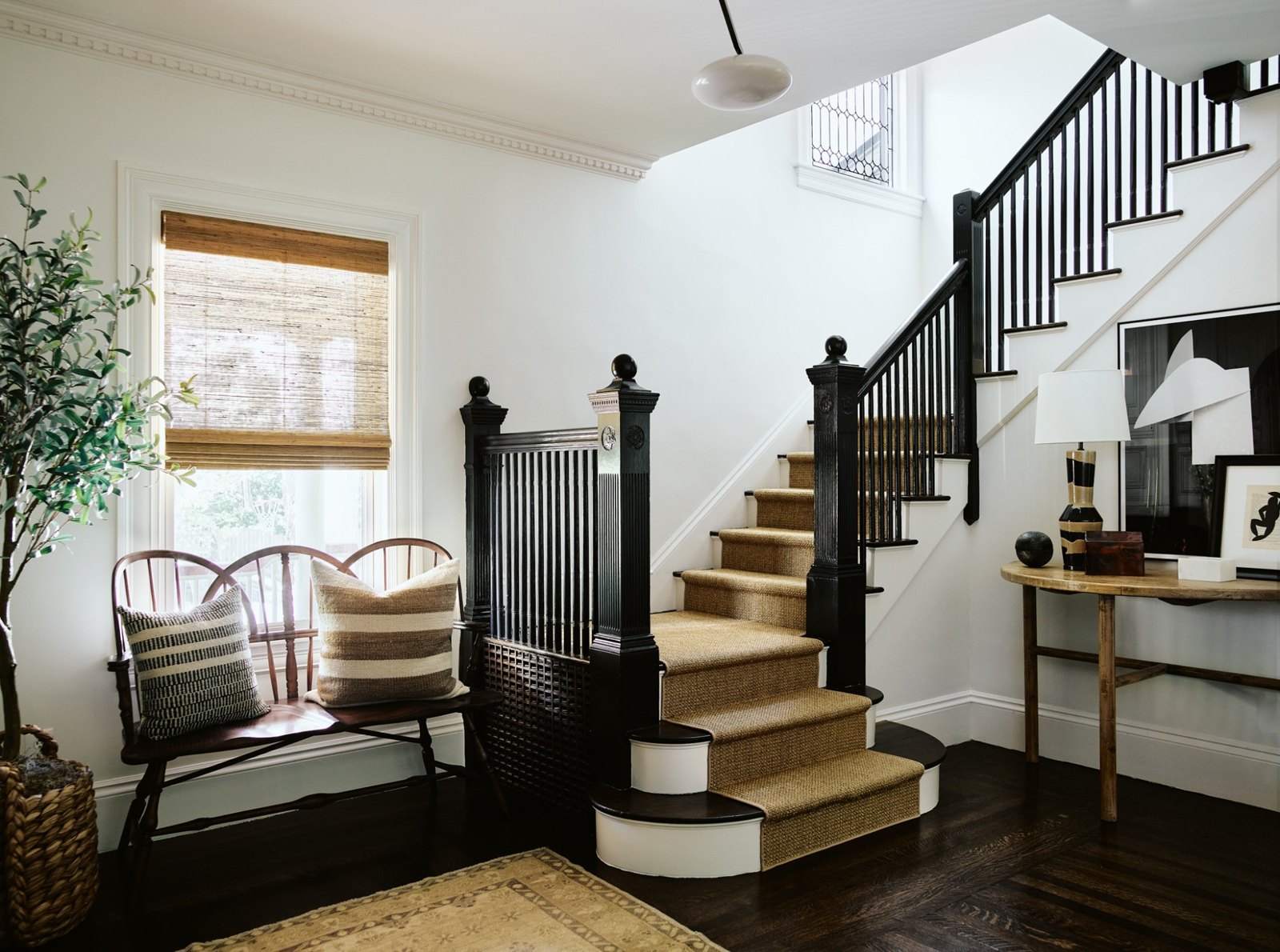 Light-filled entryway with an original dark wood staircase and woven stair runner