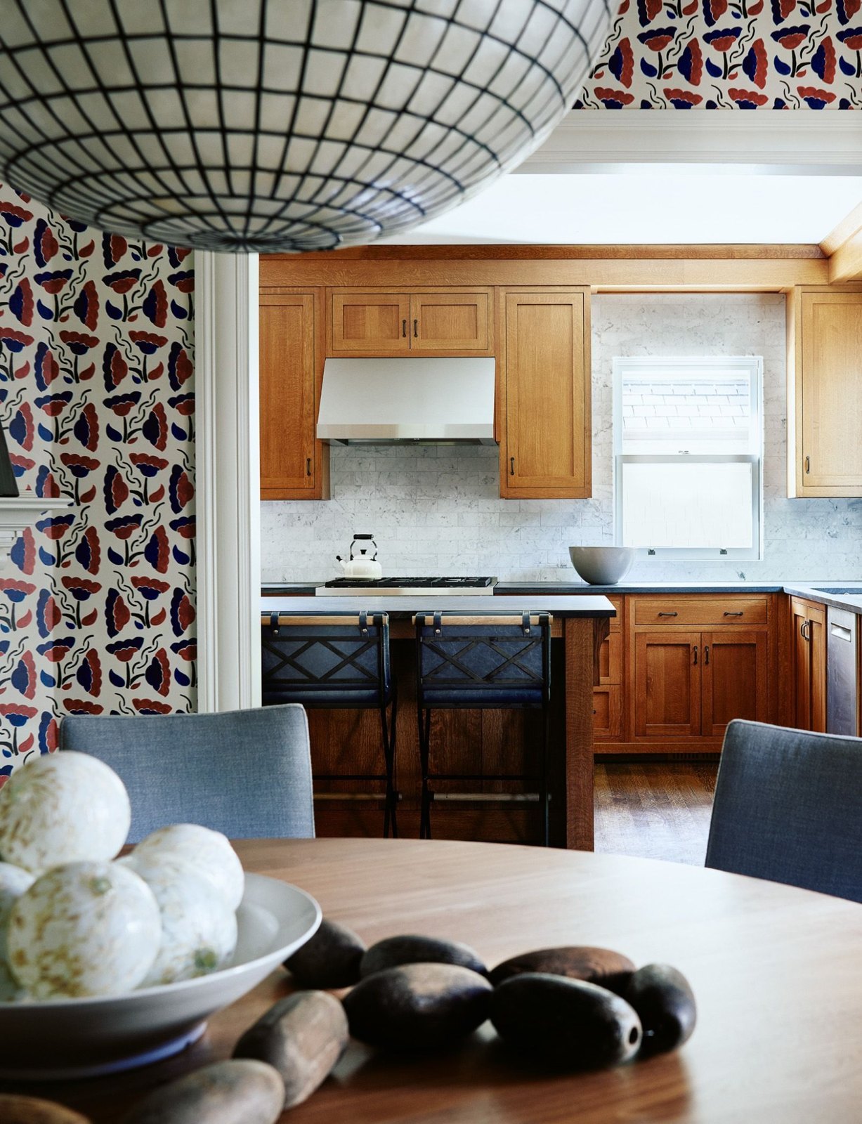 Warm wood kitchen viewed through a dining room with patterned wallpaper